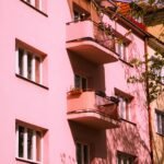 A pastel pink apartment building exterior with balconies, captured under clear daylight, showcasing an urban residential area.